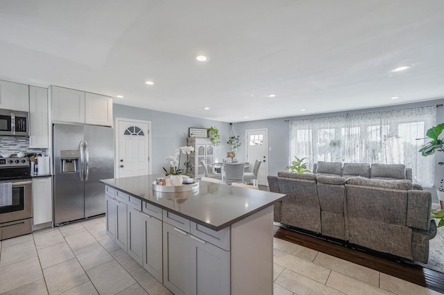 kitchen with appliances with stainless steel finishes, gray cabinetry, backsplash, a kitchen island, and light tile patterned flooring