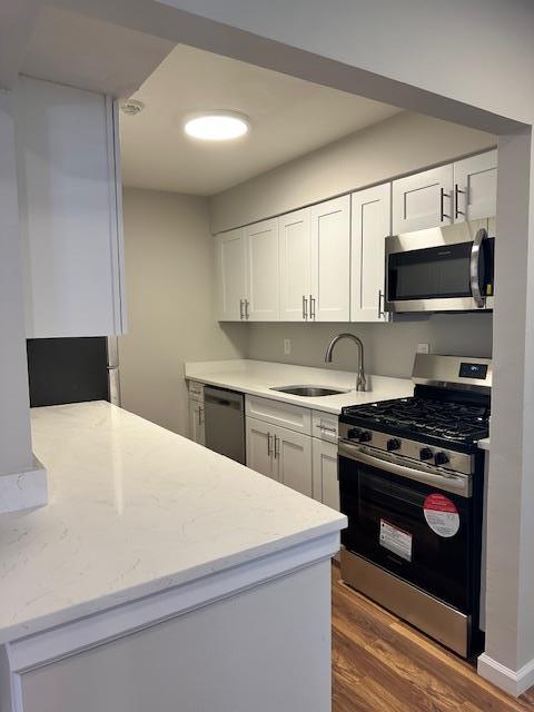 kitchen with dark wood-type flooring, sink, stainless steel appliances, light stone countertops, and white cabinets