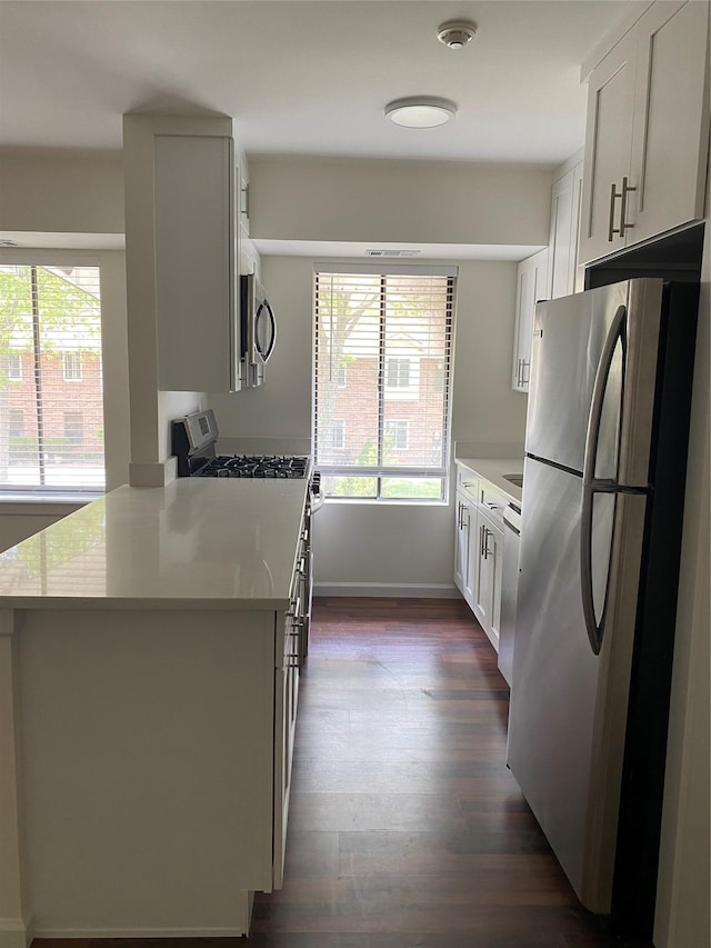 kitchen with a healthy amount of sunlight, appliances with stainless steel finishes, kitchen peninsula, and white cabinets