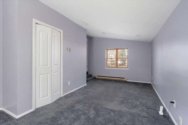 spare room with baseboard heating, lofted ceiling, and dark colored carpet