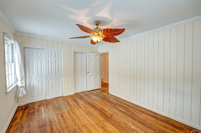 unfurnished bedroom with ornamental molding, two closets, ceiling fan, and light hardwood / wood-style floors