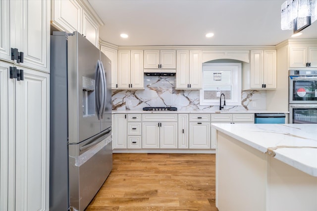 kitchen featuring appliances with stainless steel finishes, tasteful backsplash, sink, light stone countertops, and light hardwood / wood-style flooring