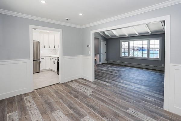 empty room with a wainscoted wall, recessed lighting, wood finished floors, and crown molding