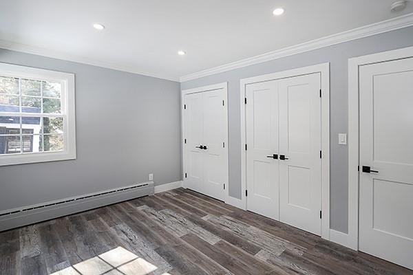 unfurnished bedroom with dark wood-style floors, a baseboard heating unit, two closets, and ornamental molding