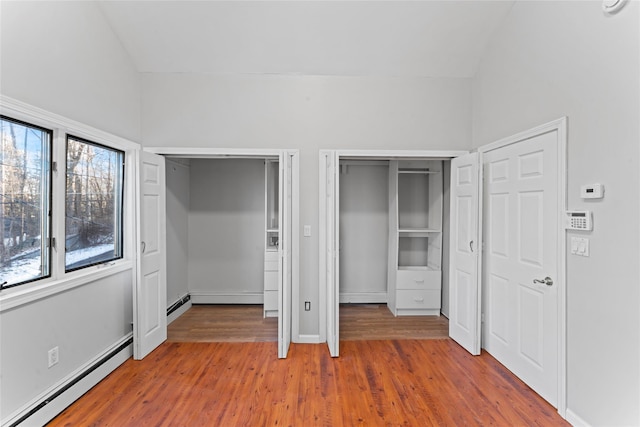 unfurnished bedroom with hardwood / wood-style flooring, a baseboard radiator, lofted ceiling, and multiple closets