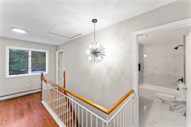 corridor with wood-type flooring, a baseboard heating unit, and a notable chandelier