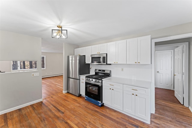 kitchen with hardwood / wood-style flooring, appliances with stainless steel finishes, white cabinets, and baseboard heating