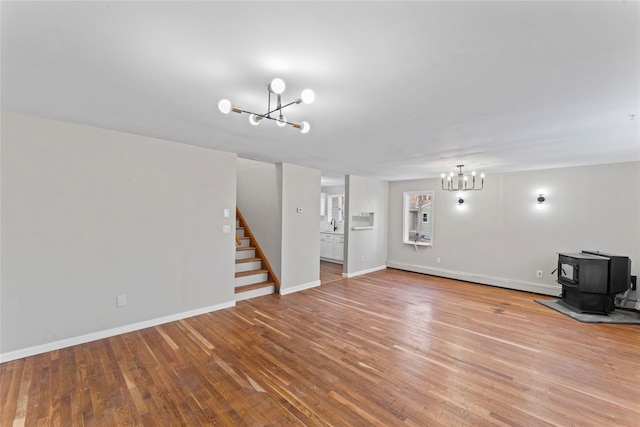 unfurnished living room featuring an inviting chandelier, a baseboard heating unit, light hardwood / wood-style floors, and a wood stove