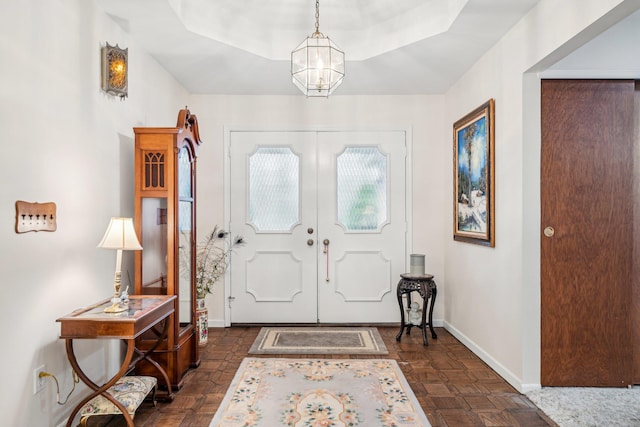 foyer entrance with french doors, a tray ceiling, and a notable chandelier