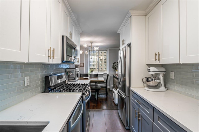 kitchen with pendant lighting, appliances with stainless steel finishes, white cabinetry, light stone counters, and tasteful backsplash