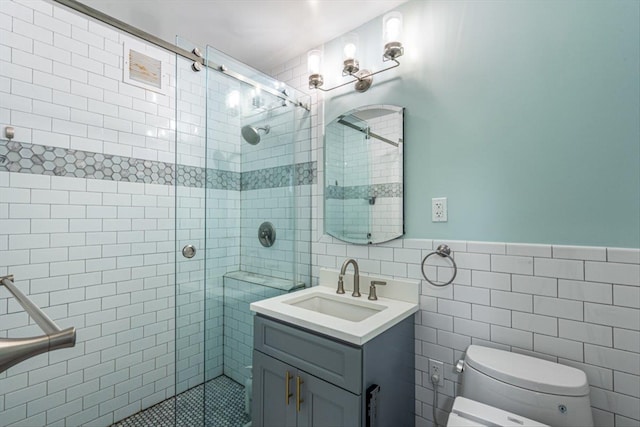 bathroom with tile walls, vanity, a shower with shower door, and toilet