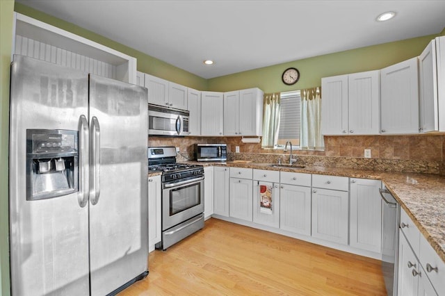 kitchen with tasteful backsplash, sink, white cabinets, light hardwood / wood-style floors, and stainless steel appliances