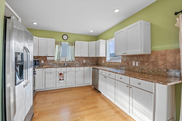 kitchen featuring sink, dark stone countertops, white cabinets, decorative backsplash, and stainless steel appliances