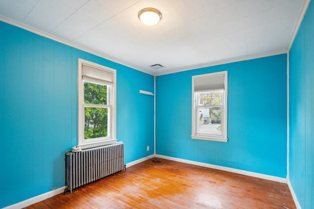 unfurnished room featuring wood finished floors, ornamental molding, baseboards, and radiator heating unit