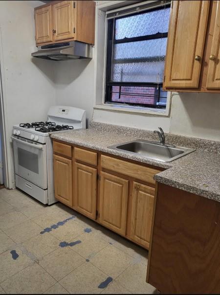 kitchen featuring under cabinet range hood, white gas range oven, and a sink