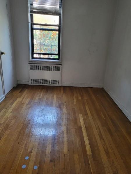 unfurnished room with hardwood / wood-style flooring, baseboards, and radiator