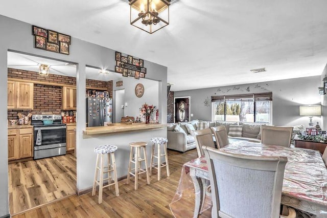 kitchen with light wood-type flooring, a breakfast bar area, brick wall, and appliances with stainless steel finishes