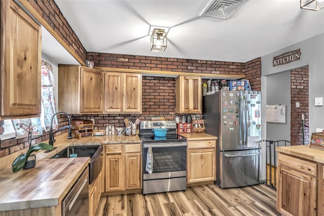 kitchen with brick wall, appliances with stainless steel finishes, light hardwood / wood-style floors, and butcher block countertops