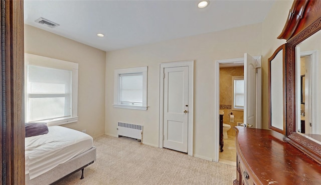 bedroom with radiator, light carpet, and ensuite bath