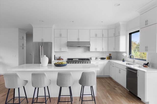 kitchen featuring sink, appliances with stainless steel finishes, white cabinetry, a center island, and ventilation hood