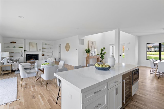 kitchen with a kitchen breakfast bar, wine cooler, white cabinets, a kitchen island, and built in microwave