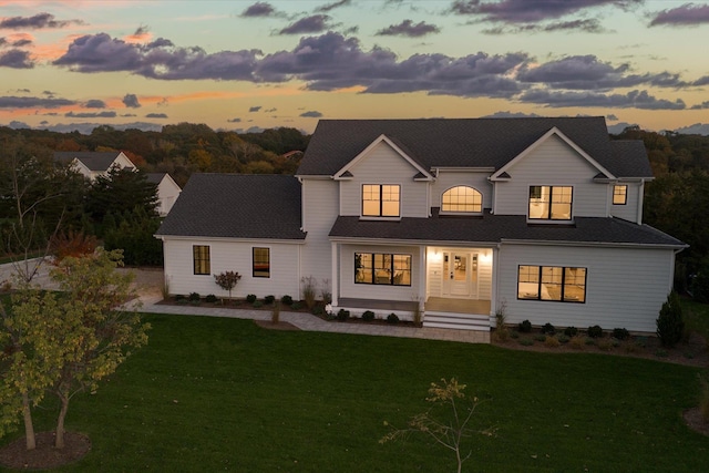 back house at dusk featuring a lawn