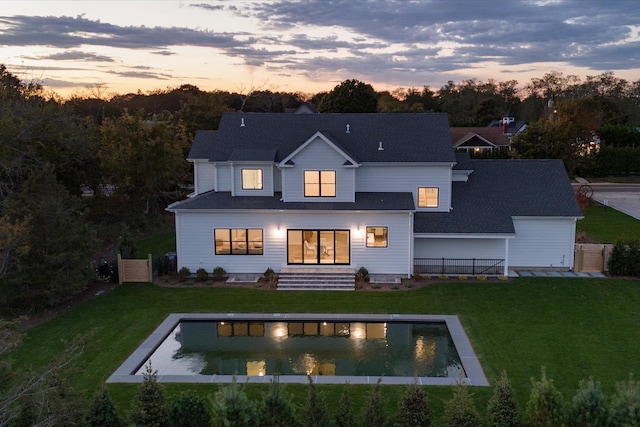 back house at dusk featuring a lawn