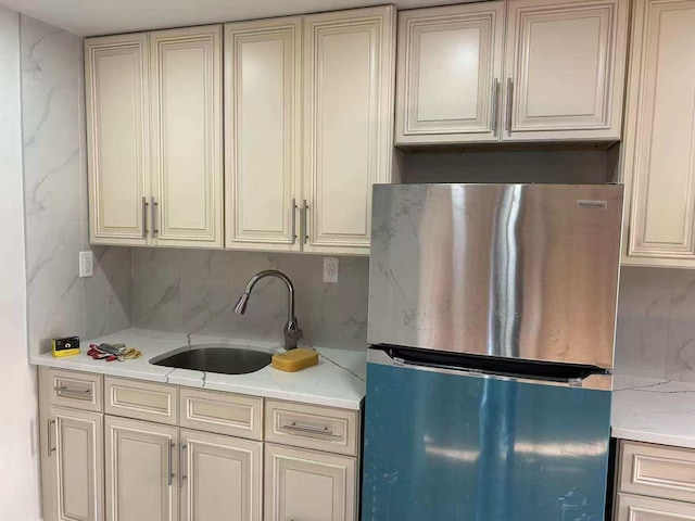 kitchen featuring sink, backsplash, cream cabinets, and stainless steel refrigerator