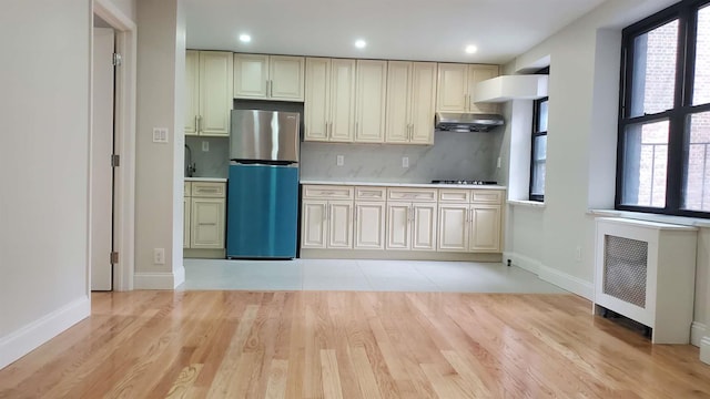 kitchen featuring under cabinet range hood, a healthy amount of sunlight, freestanding refrigerator, radiator, and tasteful backsplash