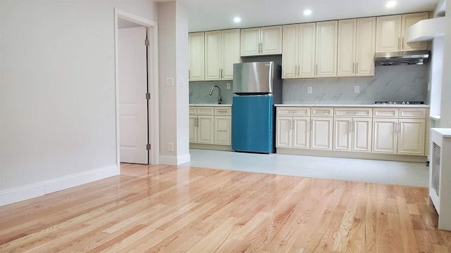 kitchen with tasteful backsplash, light countertops, freestanding refrigerator, light wood-type flooring, and under cabinet range hood