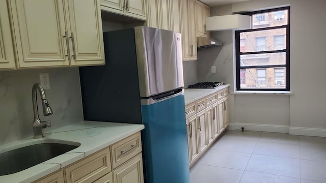 kitchen featuring light countertops, cream cabinetry, under cabinet range hood, a sink, and light tile patterned flooring