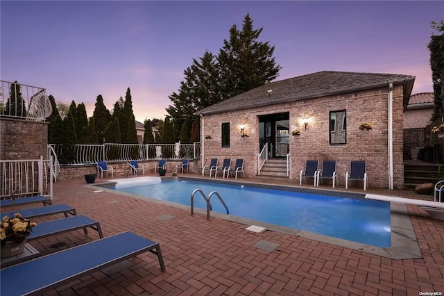 pool at dusk featuring a patio, an outdoor structure, and a diving board