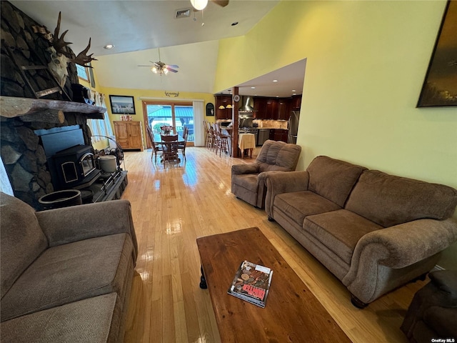 living room featuring high vaulted ceiling, a wood stove, ceiling fan, and light hardwood / wood-style flooring