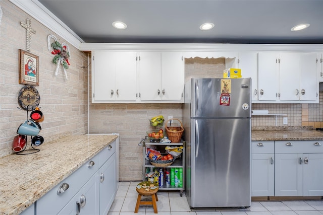 kitchen featuring light tile patterned floors, stainless steel fridge, light stone countertops, white cabinets, and decorative backsplash