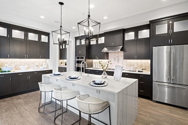 kitchen with hanging light fixtures, light wood-type flooring, appliances with stainless steel finishes, a kitchen breakfast bar, and a kitchen island with sink