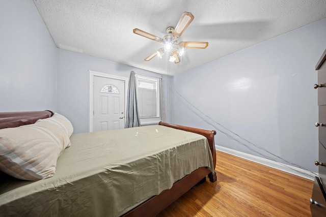 bedroom with ceiling fan, a textured ceiling, baseboards, and wood finished floors