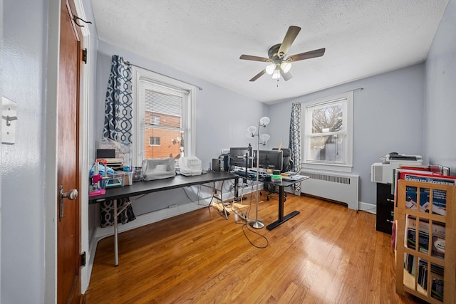 office with baseboards, radiator, hardwood / wood-style flooring, ceiling fan, and a textured ceiling