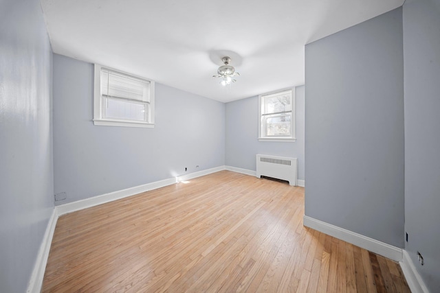 empty room with light wood-type flooring, radiator, ceiling fan, and baseboards