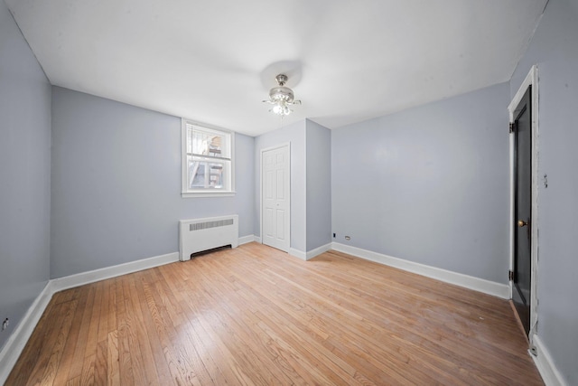 unfurnished bedroom featuring light wood-style floors, radiator heating unit, baseboards, and a closet