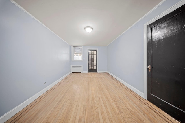 spare room with ornamental molding, radiator heating unit, light wood-style flooring, and baseboards