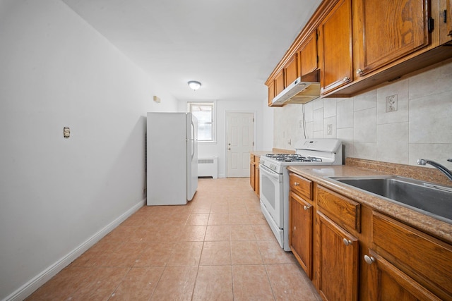 kitchen featuring brown cabinets, radiator, a sink, white appliances, and under cabinet range hood