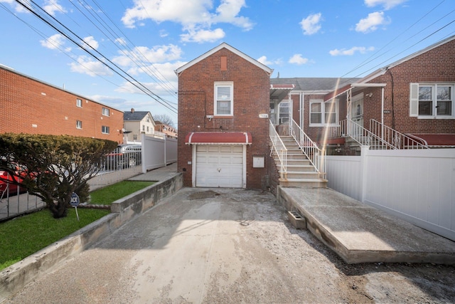 view of front facade with a garage, brick siding, driveway, and fence