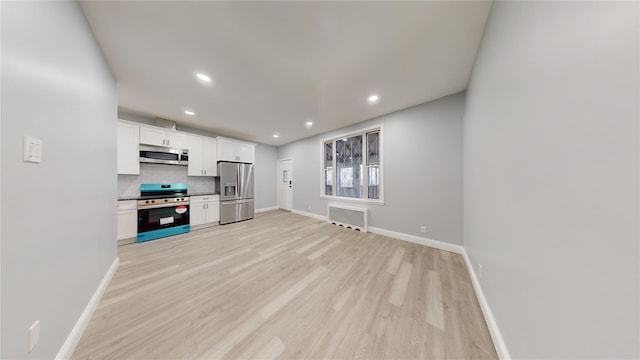 kitchen with appliances with stainless steel finishes, white cabinetry, backsplash, radiator heating unit, and light hardwood / wood-style floors