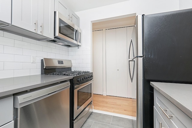 kitchen with white cabinetry, light tile patterned floors, decorative backsplash, and stainless steel appliances