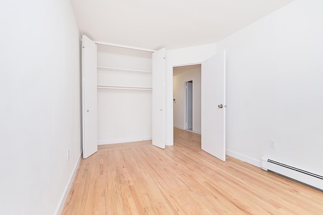 unfurnished bedroom with a baseboard heating unit, light hardwood / wood-style floors, and a closet