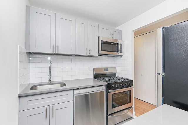 kitchen featuring appliances with stainless steel finishes, sink, light hardwood / wood-style floors, and decorative backsplash