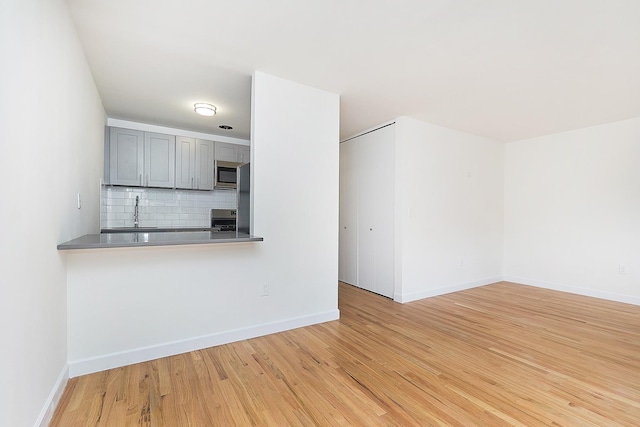 kitchen with sink, gray cabinets, appliances with stainless steel finishes, tasteful backsplash, and light wood-type flooring