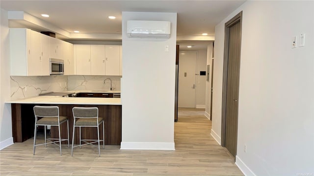 kitchen with a kitchen bar, white cabinetry, a wall mounted AC, kitchen peninsula, and backsplash