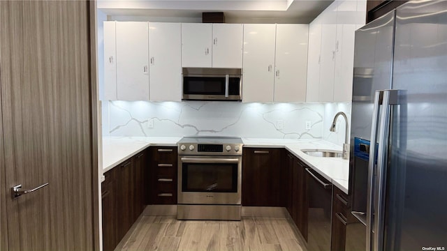 kitchen featuring sink, white cabinets, decorative backsplash, dark brown cabinetry, and stainless steel appliances