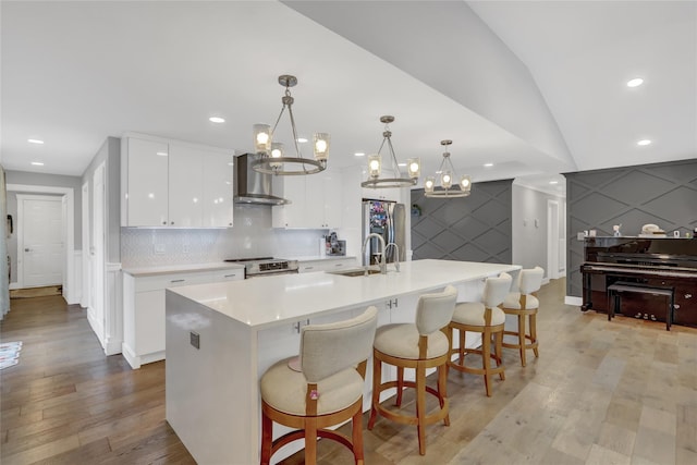 kitchen featuring white cabinets, a center island with sink, hanging light fixtures, and wall chimney range hood